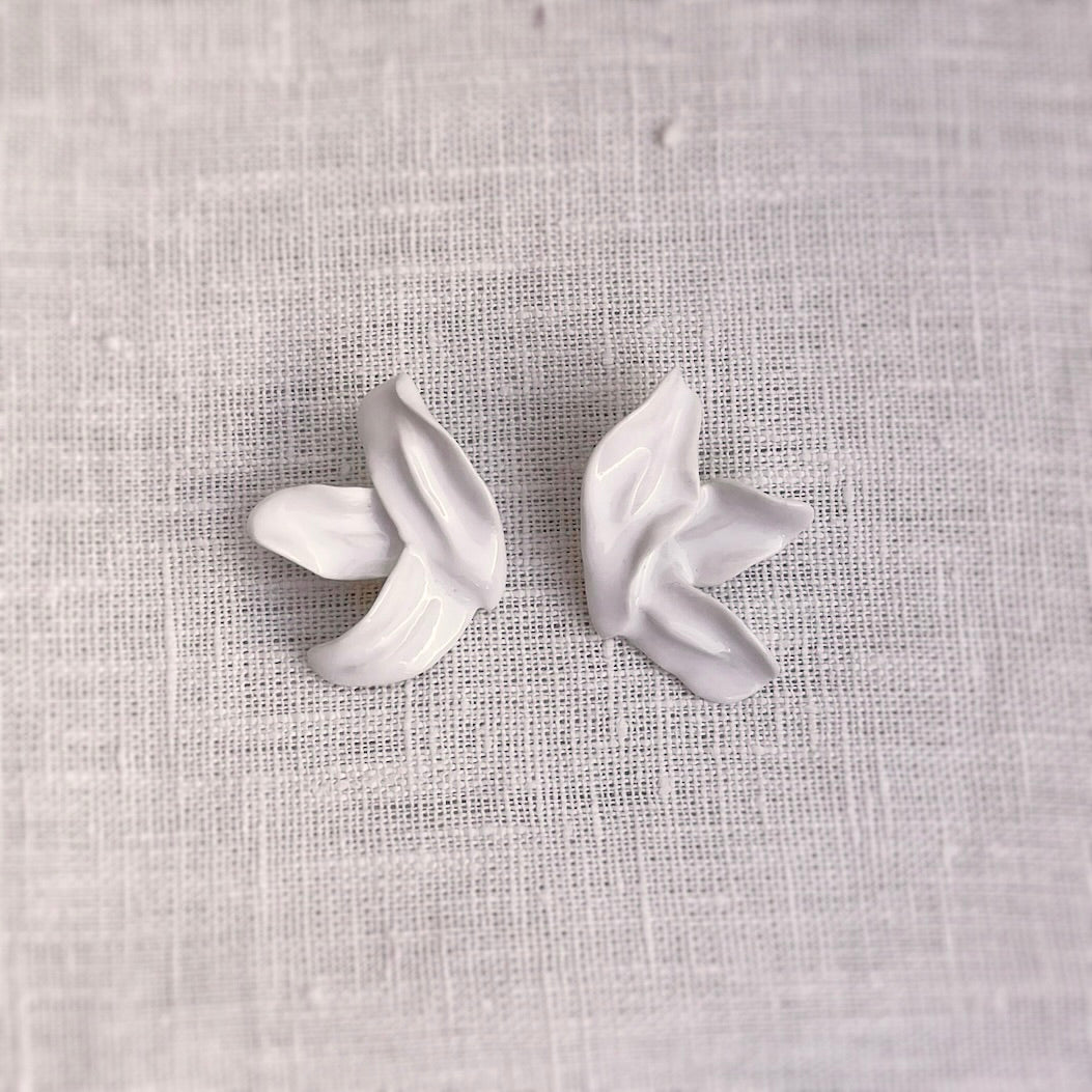 Pareja de pendientes Lilium de tres pétalos en porcelana blanca esmaltada de Maior Ceramics sobre fondo de lino